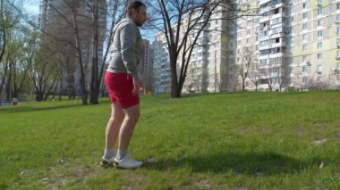 Adam parkta çimenler üzerinde fiziksel egzersiz yapıyor.