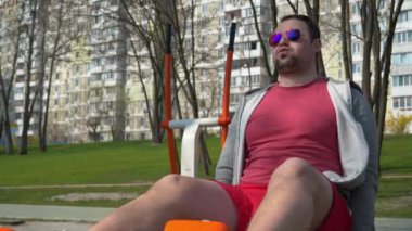 Adam spor sahasında fiziksel egzersiz yapıyor. Sporcu bacaklar için yorucu bir egzersiz yapıyor. Açık hava spor salonunda gözlüklü adam egzersizi yapıyor.