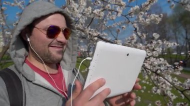 Gözlüklü tıraşsız adam tablet bilgisayar kullanıyor, ekrana bakıyor, müzik dinliyor, klip izliyor ve dans ediyor.