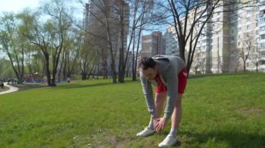 Adam parkta çimenler üzerinde fiziksel egzersiz yapıyor.