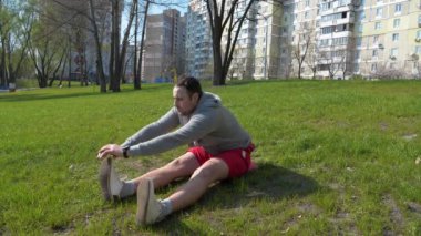 Adam parkta çimenler üzerinde fiziksel egzersiz yapıyor.