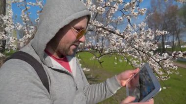 Gergin adam oyunu tablet bilgisayarda oynuyor. Tabletli kızgın adam şehir parkında kayısı ağacının yanında duruyor ve coşkuyla oynuyor, gerçeklerden kaçıyor. Tablet bilgisayarlı duygusal adam