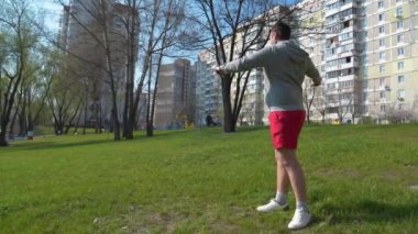 Adam parkta çimenler üzerinde fiziksel egzersiz yapıyor.