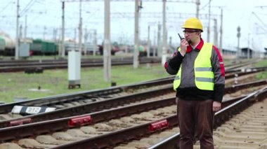 Demiryolu terminali yakınında taşınabilir telsiz vericisi olan bir demiryolu işçisi. Demiryolu çalışanı, nakliye istasyonu yakınlarındaki demiryolu hattında taşınabilir radyo vericisi aracılığıyla konuşuyor, işçi radyo istasyonu aracılığıyla iletişim kuruyor.