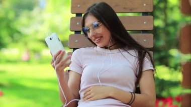 Güzel bir kadın bankta oturur ve cep telefonuyla konuşur. Akıllı telefonlu bir iş kadını halka açık bir bahçede oturur. Çekici kız cep telefonuyla konuşuyor, beyaz akıllı telefonlu bir kadın.