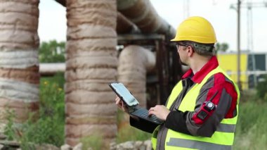 Ana boru hattının yakınındaki ısı elektrik santralinde tablet bilgisayarı olan bir işçi. Elektrik mühendisliği uzmanı sarı başlık tabletle çalışıyor.