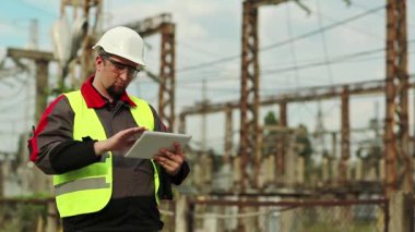 Elektrik santralinde baret takan bir işçi, mühendislik denetimi. Elektrik santralinde bilgisayarı olan bir elektrikçi. Tablet bilgisayarlı fabrika işçisi