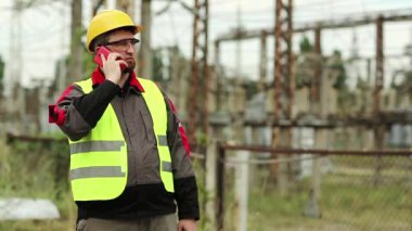 Elektrik santralinde cep telefonu ve taşınabilir radyo vericisi olan bir elektrik mühendisi. Elektrik santrali çalışanı akıllı telefondan konuşuyor