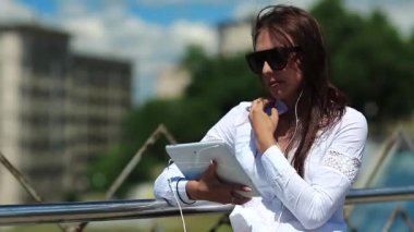 Elinde tablet bilgisayarla güneş gözlüklü çekici bir kız Skype ya da görüntülü sohbet yoluyla iletişim kuruyor. İş kadını tablet bilgisayarla iletişim kuruyor