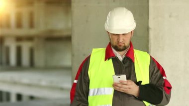 Proje alanında cep telefonu olan yeşil yelekli bir inşaatçı. İnşaat alanında akıllı telefonu olan beyaz kasklı bir işçi.
