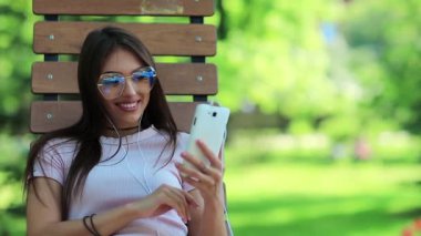 Kız şehir parkında bankta oturuyor ve akıllı telefon kullanıyor. Büyük gözlüklü bir iş kadını akıllı telefonuna bakıyor, cep telefonu olan bir kadın.
