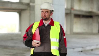 Başlıklı işçi proje sitesinde duruyor, kameraya bakıyor ve suratını ekşitiyor. İnşaat alanındaki komik inşaatçı surat yapıyor.