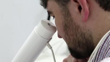 Göz hekimliği kliniğindeki hasta. Adam göz hekimliği ofisinde manyetik terapi için aletlerin içine bakıyor. Kafasında mıknatıslar var.