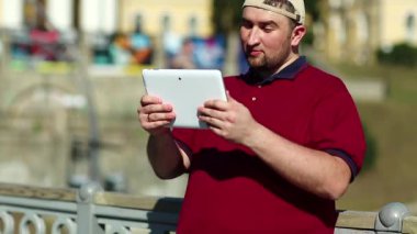 Adam tablet bilgisayarla iletişim kuruyor. Beyzbol şapkalı şişko çocuk beyaz tablet tableti tutuyor. Tabletli adam video kaset aracılığıyla iletişim kuruyor.