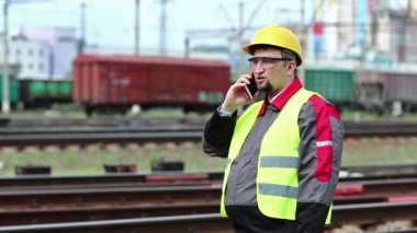 Demiryolu çalışanı cep telefonuyla konuşuyor. Demiryolu işçisi demiryolu hattında duruyor ve cep telefonuyla konuşuyor, demiryolu işçisi akıllı telefonuyla iletişim kuruyor.