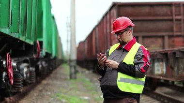 Demiryolu işçisi trenin yanında akıllı telefon kullanıyor. Demiryolu çalışanı demiryolu hattında çalışıyor cep telefonunu tutuyor, nakliye istasyonunda akıllı telefonla çalışıyor.