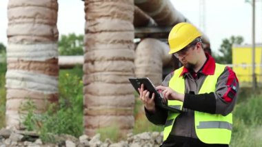 Elektrik mühendisliği uzmanı sarı başlık tabletle çalışıyor. Ana boru hattının yakınındaki ısı elektrik santralinde tablet bilgisayarı olan bir işçi.