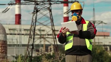 Elektrik santralindeki tablet bilgisayarlı gaz maskeli adam. Güç mühendisliği uzmanı solunum cihazında ve sarı kasketli ve kişisel bilgisayarlı ısı santralinde çalışıyor.