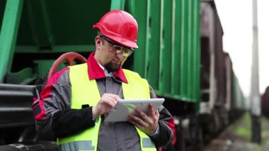 Trenin yanında tabletli bir demiryolu işçisi. Demiryolu çalışanı tablet bilgisayarla çalışır