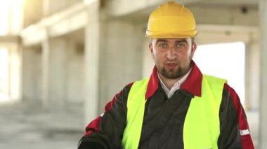 Komik işçi kamerada konuşuyor. İnşaatçı inşaat alanında durup kameraya bakar ve konuşur.