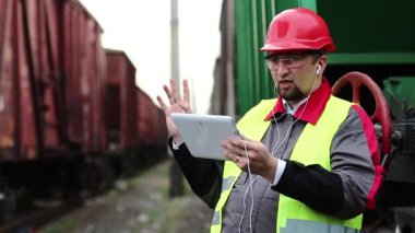 Demiryolu işçisi tablet bilgisayarla konuşuyor. Yük istasyonundaki demiryolu işçisi tablet bilgisayarla görüntülü sohbet yoluyla konuşuyor