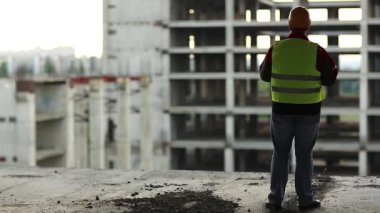 İnşaat teknolojisi uzmanı yeni yapılara bakıyor. Başlıklı işçi proje sitesinde duruyor ve yeni bina yapısına bakıyor