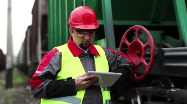 Yük treninin yanında tablet bilgisayarı olan bir demiryolu işçisi. Demiryolu çalışanı tablet bilgisayarla çalışır