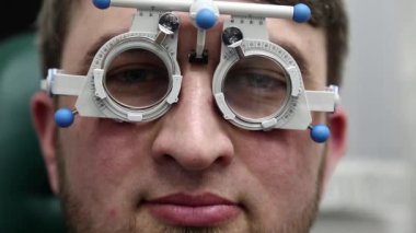 Göz doktorunun resepsiyonundaki hasta adam, göz hekimliği kliniğindeki mercek seçimi, kameraya yakından bakıyor.