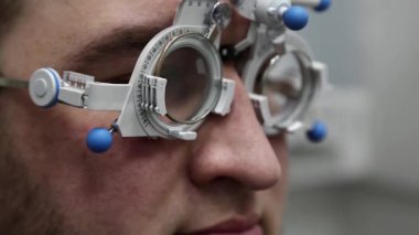Göz doktorunun resepsiyonundaki hasta adam, göz hekimliği kliniğindeki gözlük lensleri seçimi, yakından bakan adam.
