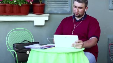 Kafedeki işadamı tablet bilgisayarla konuşuyor. Şişman adam yaz restoranında masada oturuyor ve tablet bilgisayar, akıllı telefon ve iş evrakları üzerine konuşuyor.