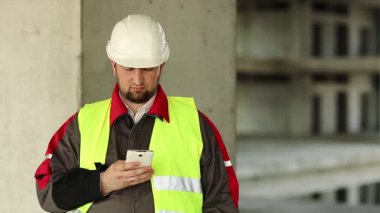 Proje alanında cep telefonu olan yeşil yelekli bir inşaatçı. İnşaat alanında akıllı telefonu olan beyaz kasklı bir işçi.