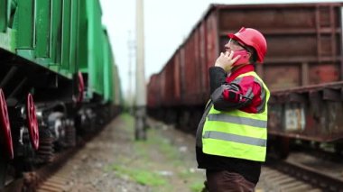 Demiryolu çalışanı demiryolu hattında çalışıyor. Cep telefonuyla konuşuyor. İşyerinin müdürü, nakliye istasyonundaki akıllı telefondan iletişim kuruyor. Demiryolu işçisi tren yakınlarında cep telefonuyla konuşuyor.