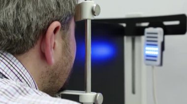 Dinamik fototerapi için bir cihaz. Optalmoloji kliniğindeki hasta, adam göz doktoru odasındaki dinamik fototerapi cihazına bakıyor, ışık tedavisi görüyor.