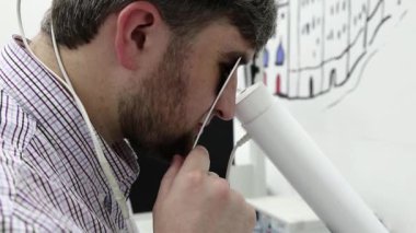 Göz bilimi kliniğindeki adam. Hasta göz doktorunun ofisinde manyetik terapi için aletlerin içine bakıyor. Kafasında mıknatıslar var.