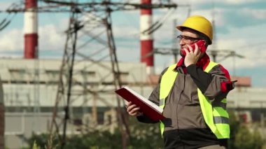 Elektrik mühendisliği uzmanı, sarı başlıklı, cep telefonlu ve elektrik santralinde çalışan biri. Elektrik santralindeki işçiler akıllı telefondan konuşuyor