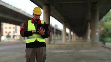 Tamirhanenin müdürü, inşaat alanında çalışıyor. Ana yolun altında. Bilgisayarına veri giriyor. Üst geçidin altında kişisel bilgisayarı olan bir işçi