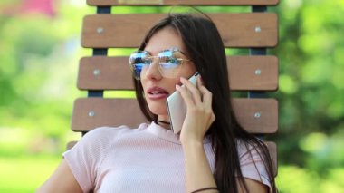 Güzel bir kadın bankta oturur ve cep telefonuyla konuşur. Akıllı telefonlu bir iş kadını halka açık bir bahçede oturur. Çekici kız cep telefonuyla konuşuyor, beyaz akıllı telefonlu bir kadın.