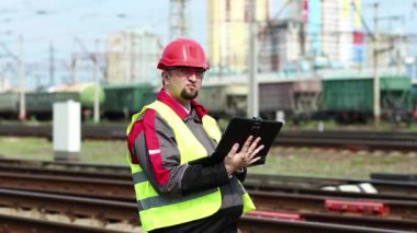 Tren terminalinde bilgisayarı olan bir demiryolcusu. Üniformalı ve kırmızı şapkalı demiryolu işçisi tablet bilgisayarla çalışıyor. Demiryolu çalışanı tabletine notlar alıyor.