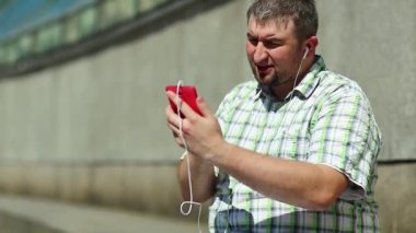Komik adam akıllı telefondan konuşuyor. Akıllı telefonlu neşeli adam Skype üzerinden iletişim kuruyor ve el kol hareketi yapıyor. Elinde kırmızı cep telefonu olan, kareli tişörtlü, şişman, şen şakrak adam.