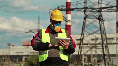 Elektrik mühendisliği uzmanı, solunum cihazı ve sarı başlık. Isı santralinde kişisel bilgisayarı var. Elektrik santralinde tablet bilgisayarlı gaz maskeli güçlü adam.