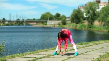 Göl kenarında fiziksel egzersiz yapan bir kadın. Kırmızı spor ceketli kız sabah egzersizleri yapıyor. Fiziksel aktivite kalorileri yakmaya yardımcı olur. Kız spora gider, kız spor yapar.