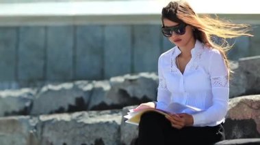 Ticari evrakları olan kızgın ve stresli bir kadın. Sinirli genç kadın şehir merkezindeki büyük merdivenlerde oturuyor ve elinde iş belgeleriyle geziyor, rüzgar ona esiyor.