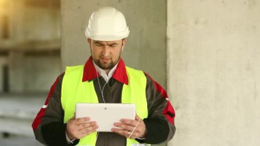 İnşaatçı proje sitesindeki tablet bilgisayarla konuşuyor. İnşaat alanında tablet bilgisayarı olan bir işçi. Beyaz başlıklı işçi elinde kişisel bilgisayarla, ekranda görünüyor.