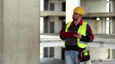 Usta inşaatçı çalışma belgelerine notlar alır. İnşaat müfettişi proje alanında çalışma belgeleriyle birlikte.