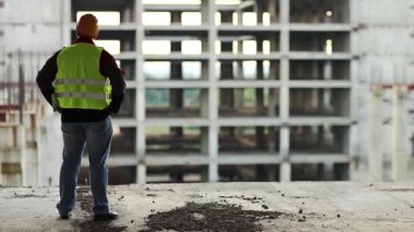 İnşaatçı yeni yapılara bakıyor. Başlıklı işçi proje sitesinde duruyor ve yeni bina yapısına bakıyor