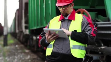 Yük treninin yanında tablet bilgisayarı olan bir demiryolu işçisi. Demiryolu çalışanı tablet bilgisayarla çalışır