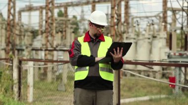 Elektrik santralinde bilgisayarı olan bir elektrikçi. Elektrik santralinde baret takan bir işçi, mühendislik denetimi. Tablet bilgisayarlı fabrika işçisi