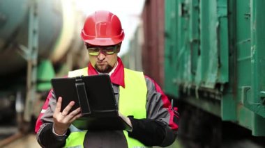 Yük istasyonundaki demiryolu trafiği müfettişi tabletine not alıyor. Trenler arasında tablet bilgisayarı olan demiryolu işçisi.