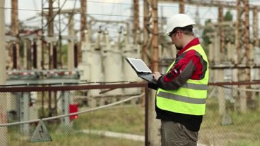 Elektrik santralinde bilgisayarı olan bir elektrikçi. Elektrik santralinde baret takan bir işçi, mühendislik denetimi. Tablet bilgisayarlı fabrika işçisi