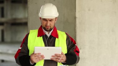 İnşaatçı proje sitesindeki tablet bilgisayarla konuşuyor. İnşaat alanında tablet bilgisayarı olan bir işçi. Beyaz başlıklı işçi elinde kişisel bilgisayarla, ekranda görünüyor.